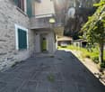 2-story stone house with green shutters, stone patio, garage, and surrounding greenery