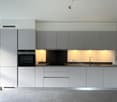 Modern kitchen with grey cabinets, integrated appliances, granite countertop, stainless steel sink and faucet, and a black stove and oven.