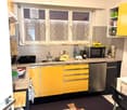 modern kitchen with yellow cabinets, granite countertop, undermount sink, stainless steel dishwasher, microwave, kettle, refrigerator, and window with curtains