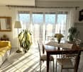 Dining room, yellow couch, wooden table, chairs, plants, radiator, picture frame, mirror, lamp, clock