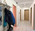A hallway with tiled floor, wooden doors, a wooden coat rack with jackets and shoes, a mirror, and a picture frame on the wall.