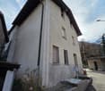 2 story house, concrete wall, windows with metal grills, chimney, plants in front