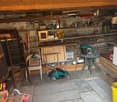 A storage room with wooden ceiling, shelves, ladder, table, chair, and various items