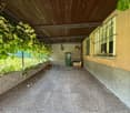 covered walkway with stone floor, wooden ceiling, green trash bin, broom, plants, and a window with bars