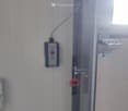 Automatic garage door control panel with red button and arrows mounted on white wall, metal hinge, red hook hanging