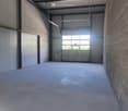 white walls, ceiling with metal beams, roller door, floor with concrete texture, bright light coming from outside