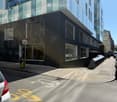 Modern building with glass windows, black exterior, located on a street with parked cars