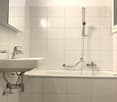 Modern, clean, white tiled walls and floor, large mirror, faucet, white sink, bathtub, shower area with grab bars