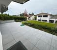 Outdoor tile flooring, grassy lawn, green hose, white wall, garden plants, fence, houses