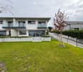 Modern white two-story house, glass balconies, concrete front yard, large green lawn