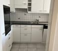 modern white kitchen with grey tiles, black countertops, oven, dishwasher, sink with faucet, dishwasher machine, built-in cabinets, drawers