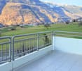 Outdoor terrace with white tiled flooring, metal railing, view of a grassy field and mountains