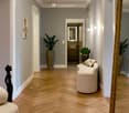 Wide hall with wooden floor, walls painted gray, white furniture and plant on the floor, mirror on the wall