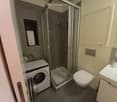 modern bathroom with shower stall, white toilet, sink, built-in cabinet, private washing machine