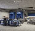 Industrial workshop with blue cabinets, workbenches, and overhead lighting.