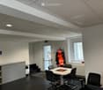 Office space with a round table, chairs, coffee machine, coat rack, and shelves.