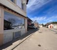 Building with a glass storefront, white shutters, and a garage with cars parked in front.