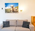 A living room with a gray couch, two pillows, a wooden cabinet, a wall-mounted photo, and a wall lamp.