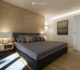 Modern bedroom with wooden floor, textured wall, bed, nightstands, lamps, rug, and artwork.
