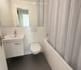 Modern bathroom with white tiles, a sink, toilet, bathtub, and a large mirror above the sink.