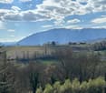 Garden / Outdoor Area. A panoramic view of a rural landscape with cultivated fields, scattered trees, and distant snow-capped mountains under a partly cloudy sky.