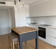 Modern kitchen with white cabinets, wooden island, two stools, built-in oven, sink, and pendant lights.