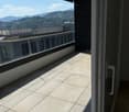 Spacious balcony with tiled floor, large glass sliding doors, and a scenic view of mountains and cityscape.