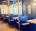 Restaurant interior with wooden tables, benches, and chairs arranged around birch tree trunks, warm lighting, and wooden flooring.