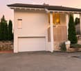 House. Modern two-story house with white exterior, garage, large windows, and landscaped garden with coniferous trees.