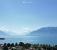 Panoramic view of a lake surrounded by mountains, with a town and houses visible on the shore.