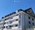 Modern multi-story residential building with white facade, multiple balconies, and a flat roof with small dormer windows.
