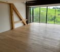 Unfurnished Room. Empty room with wooden beams, wooden floor, and large glass windows leading to a balcony with a view of a green landscape.