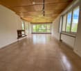 Empty room with tiled floor, large windows, fireplace, and wooden ceiling.