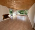 Empty room with tiled floor, fireplace, large windows, and sliding glass doors leading to a garden.