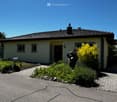 Single-story house with beige walls, dark roof, small garden, and driveway.