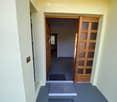 A clean, well-lit hallway with a tiled floor, white walls, and wooden doors leading to other rooms.