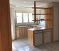 Empty kitchen with wooden cabinets, tiled floor, and a central island with built-in appliances. Large windows provide natural light.