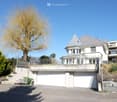 Two-story house with a garage, raised ground floor, and a balcony overlooking the street.