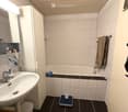 Modern bathroom with white tiles, a sink with a mirror cabinet, a bathtub, a towel on a rack, and a scale on the floor.