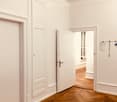Empty hallway with white walls, wooden herringbone flooring, and two doors leading to other rooms.