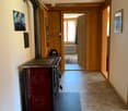 A hallway with wooden paneling, a red wood-burning stove, and a blue mat. The hallway leads to another room with a visible rug and radiator.