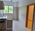 Empty kitchen with tiled floor, white walls, and a window overlooking a green area. Basic cabinetry and sink are present, but no appliances or furniture.