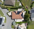 Aerial view of a residential area with multiple houses, solar panels on roofs, gardens, driveways, and parked cars.