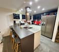Modern kitchen with a central island, bar stools, stainless steel appliances, and a red backsplash.