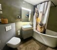 Modern bathroom with a white toilet, bathtub, sink, and mirror. Features a decorative wicker basket on a shelf and a stylish shower curtain with an abstract design.