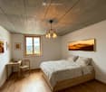 Cozy bedroom with wooden bed, desk, chair, and large window overlooking a scenic landscape.
