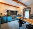 Modern kitchen with blue cabinets, stainless steel appliances, wooden island, bar stools, and fruit bowl on counter.