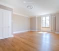 Empty room with wooden flooring, white walls, large window, and white door.