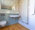 Modern bathroom with a white toilet, sink, large mirror, and radiator. Blue tiled walls and wooden flooring.