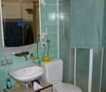 Bathroom with green tiled walls, a white sink, a toilet, a shower with a glass enclosure, and a mirror above the sink. The sink has a faucet, and there are various toiletries and a towel visible.